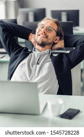 Young man is trying to relax while listening to music at work. Coffee cup and a computer visible in the foreground.