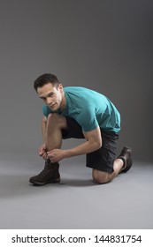 Young Man Tying The Laces Of Shoes Over Gray Background