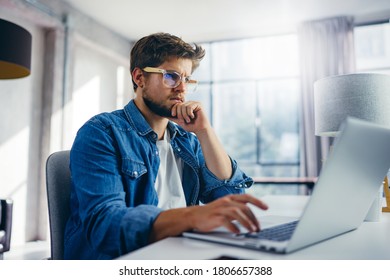 Young man typing on laptop. Modern businessman at sunny office. Freelancer at work. Blogger or journalist writing new article - Shutterstock ID 1806657388