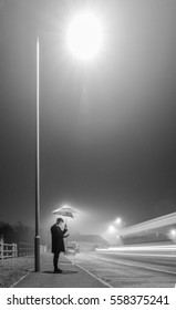 Young Man Under Street Lamp With Umbrella On Foggy Evening