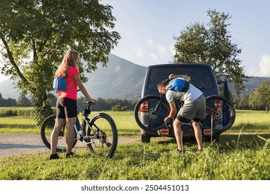 Young man is unloading electric mountain bikes, for himself and his girlfriend, lifting them from the hitch rack on the vehicle. - Powered by Shutterstock