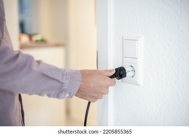 Young Man Unplugging Power Cord At Home