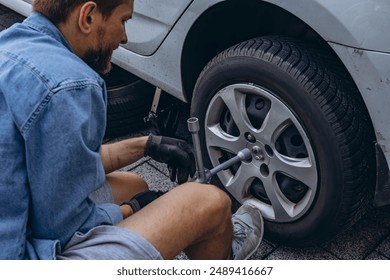 Young man in unscrewing lug nuts on car wheel in process of new tire replacement,using wrench while changing flat tire on the road. High quality photo - Powered by Shutterstock