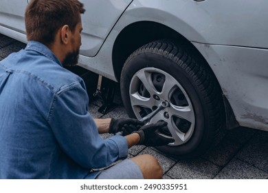 Young man in unscrewing lug nuts on car wheel in process of new tire replacement,using wrench while changing flat tire on the road. High quality photo - Powered by Shutterstock