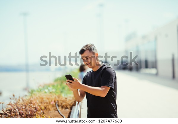 Young man use mobile phone in airport outdoors\
with plane on background