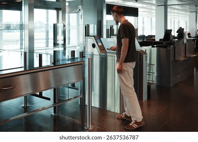 A young man uses her smartphone to scan a boarding pass at an automated airport gate. Concept of digitalization, self-check-in and independent travel.