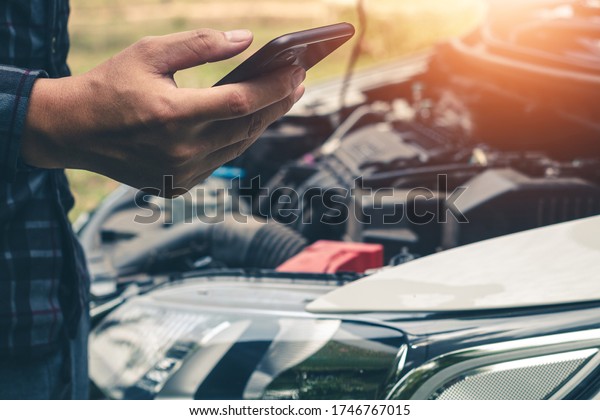 Young man uses a mobile phone to\
call the mechanic while looking at broken down car on\
road.