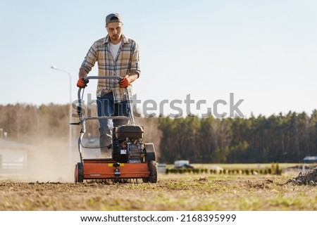 Young man using aerator machine to scarification and aeration of lawn or meadow