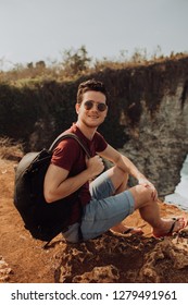 Young man using a backpack on top a ocean cliff, happy smiling emotions