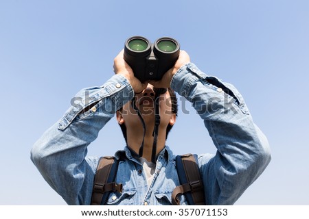 Young Man using binoculars with clear blue sky