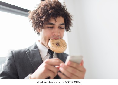 Young man using cell phone with bagel in mouth - Powered by Shutterstock