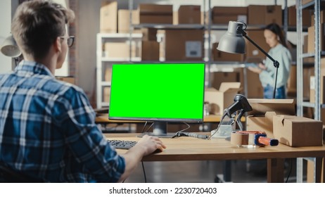 Young Man Using Desktop Computer with a Green Screen Chromakey Mock Up Display. Distribution Manager and Employee Working in Distribution Warehouse with Cardboard Boxes. Over the Shoulder Footage. - Powered by Shutterstock - Get 15% off with code: PIKWIZARD15