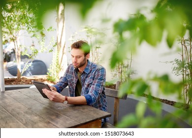 Young Man Using A Digital Tablet To Browse The Internet While Sitting Outside At A Table On A Patio 