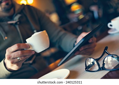 Young Man Using Digital Tablet And Drinking Coffee In Cafe