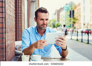 Young man using digital tablet at outdoors cafe on city street - Powered by Shutterstock