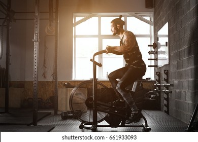 Young Man Using Exercise Bike At The Gym. Fitness Male Using Air Bike For Cardio Workout At Crossfit Gym.