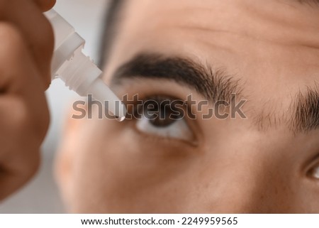 Young man using eye drops at home, closeup