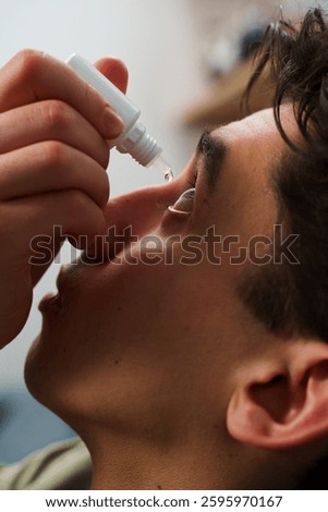 Young man is using eye drops for irritation problem. Man is applying medical eye drops from eye wellnesses at home