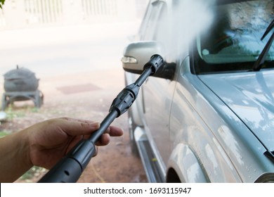 The Young Man Is Using A High Pressure Water Gun To Wash The Car.