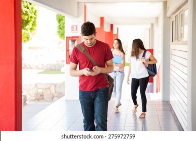 Young man using his cell phone for texting while walking on a school hallway