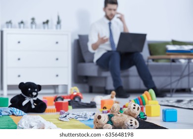 Young man using his laptop and calling on a sofa in messy nursery