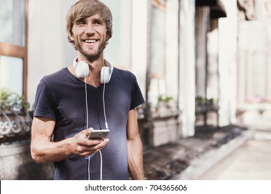 Young Man Using His Smartphone In The City. Close Up Of Cheerful Adult Typing On Mobile Phone Outdoors