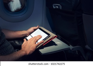 Young man using his tablet on a plane during a flight. This guy's reading an e-book. Electronic book. pastime during the flight on Board the aircraft - Powered by Shutterstock