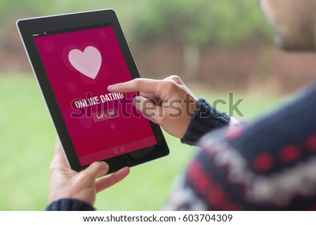 A young man is using his tablet in a green nature background, with online dating app on screen