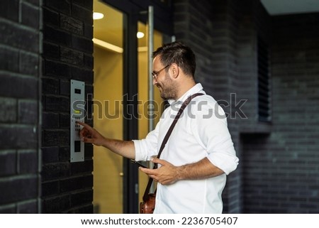 Young man using intercom at residential building entrance. People and business concept.