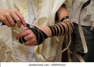 A young man using a Jewish Tefillin on his arm and wearing prayer shawl for praying