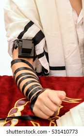 A young man using a Jewish Tefillin on his hand and wearing prayer shawl for praying