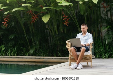 Young man using a laptop computer in a garden with a swimming pool. business, study, freelance - Powered by Shutterstock