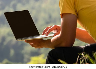 Young Man Using Laptop Computer, Notebook Outside In Nature Against Background Of Mountain Forest. Online Remote Working And Learning. Copy Space For Design Or Text On Laptop Black Screen