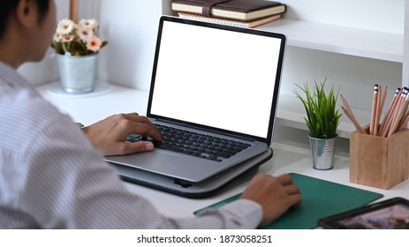 Der junge Mann, der Laptop nutzt, kontaktiert Geschäftsinformationen auf dem Schreibtisch im Büro. Leerer Bildschirm für Werbetext.