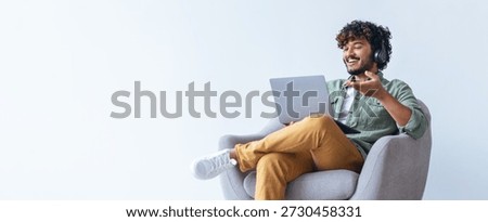 Young Man Using Laptop in Cozy Chair While Wearing Headphones During Online Meeting