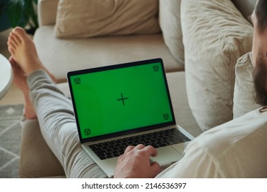 Young Man Using Laptop Green Screen Chroma Key, Working With Touch Pad, Lying On Sofa At Home