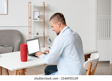 Young Man Using Laptop On Table With Wireless Portable Speaker In Room