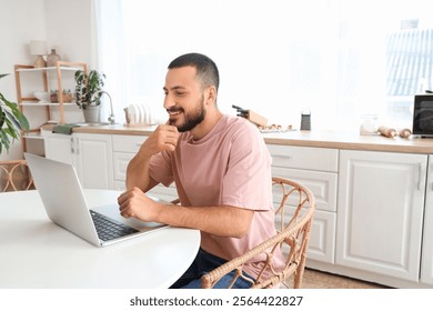 Young man using laptop at table in kitchen
