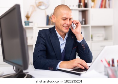 Young man using laptop and talking by phone at the office table