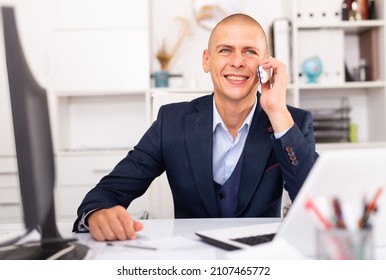 Young man using laptop and talking by phone at the office table