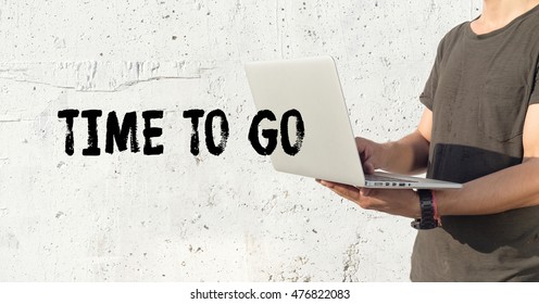 Young man using laptop and TIME TO GO concept on wall background