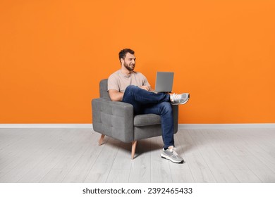 Young man using laptop while sitting in armchair indoors
