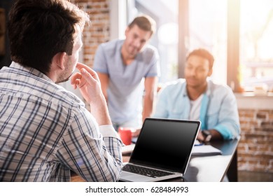 Young man using laptop while colleagues discussing project, small business meeting concept