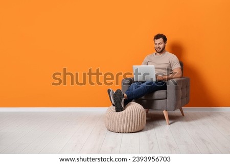 Young man using laptop while sitting in armchair indoors. Space for text