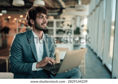 Young man using laptop while sitting in a contemporary office, a confident professional planning his ambitious career
