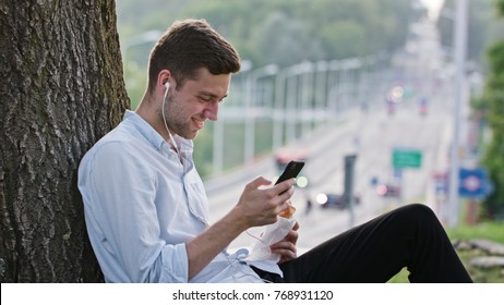 A young man using a mobile and having a snack outdoors. Medium shot. Soft focus.