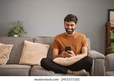 Young man using mobile phone while relaxing on sofa in living room - Powered by Shutterstock