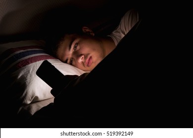 Young Man Using Mobile Phone On Bed In The Dark