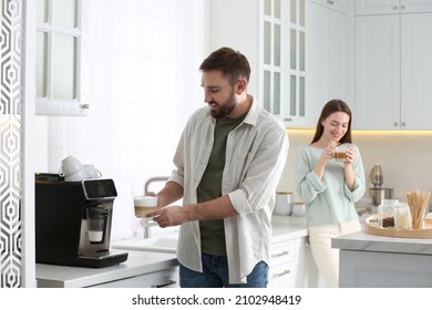 Young Man Using Modern Coffee Machine In Kitchen