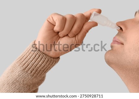 Young man using nasal drops on light background, closeup